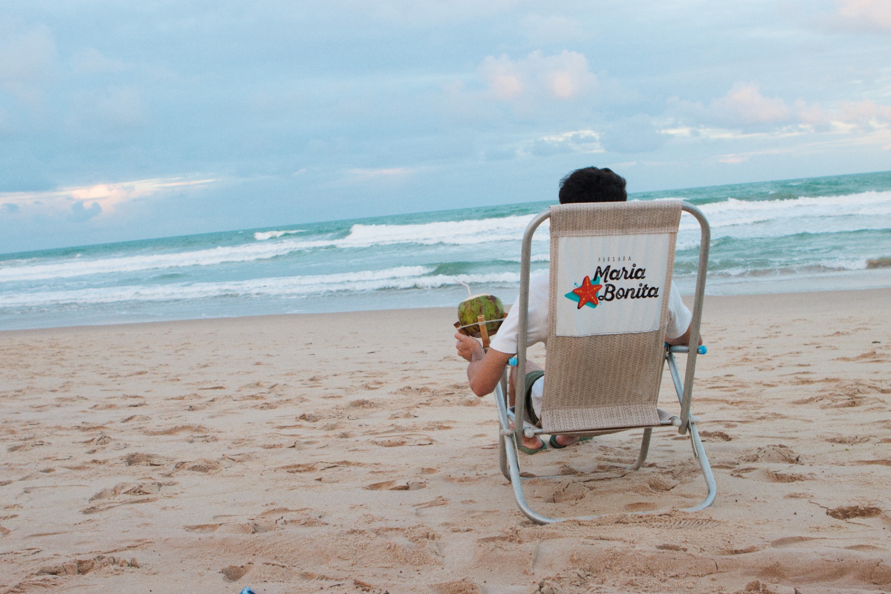 Hóspede relaxando na cadeira de praia com água de coco